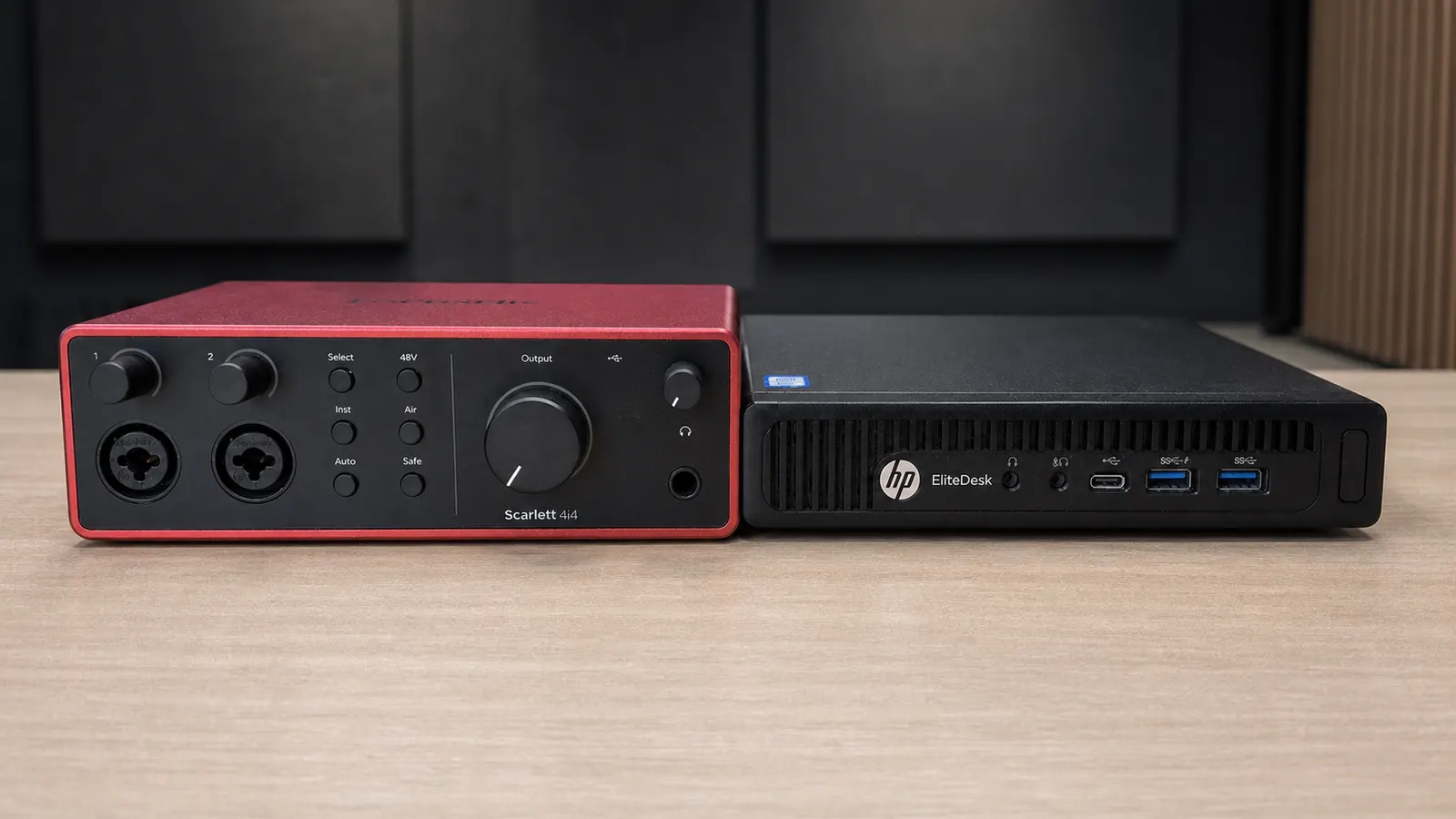 Une interface audio Focusrite Scarlett 4i4 posée à côté d'un mini PC HP EliteDesk, sur un plan de travail, devant des panneaux acoustiques