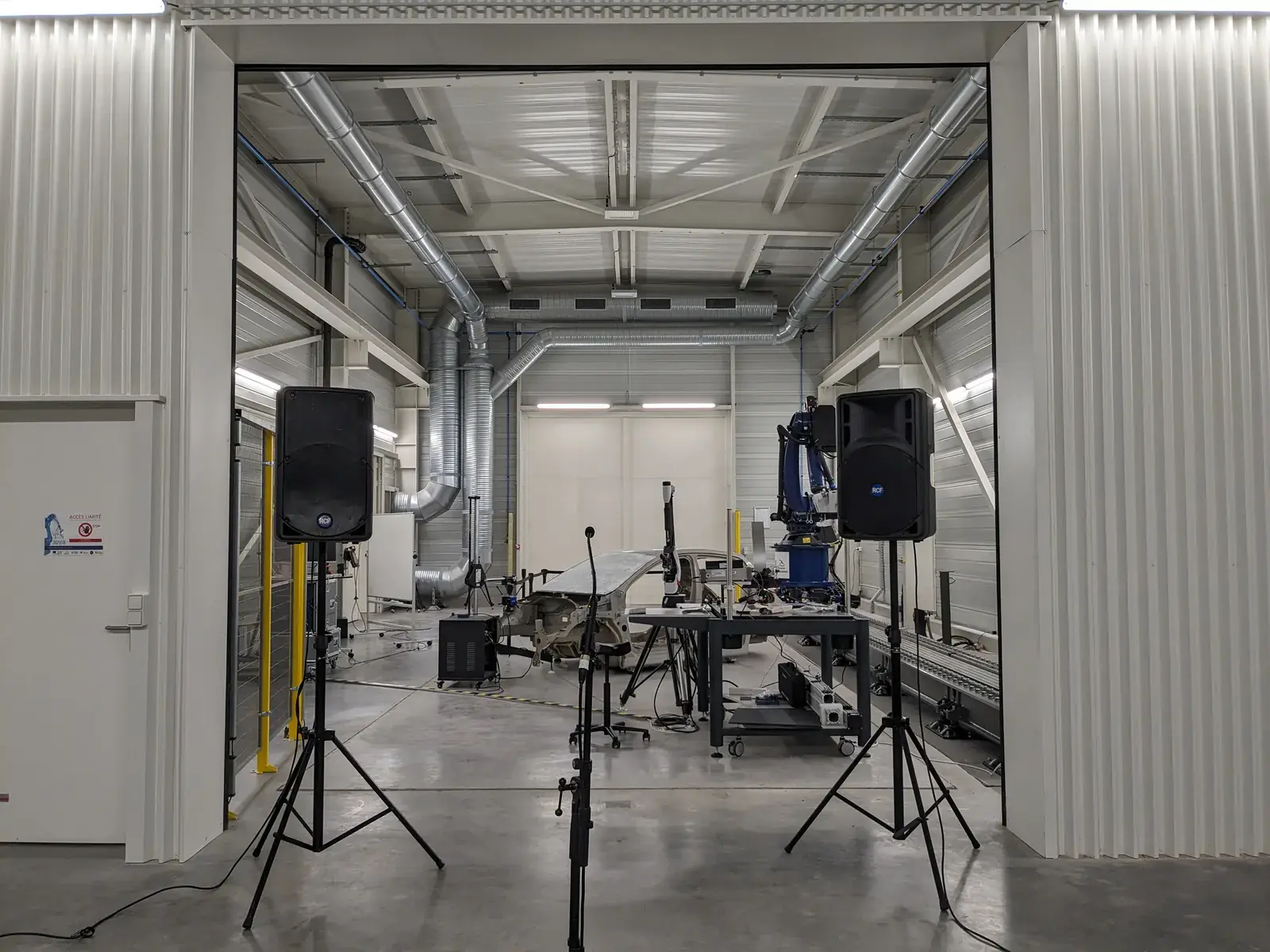 Halle d'essais industrielle, deux enceintes sur pieds, pied de microphone, pièce en cours de caractérisation