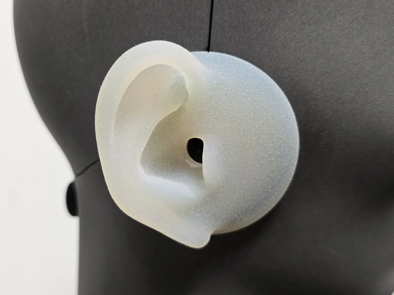 Oreille en silicone blanc d'une tête artificielle de mesure, vue de côté, avec l'entrée du conduit auditif au fond duquel se trouve le microphone de mesure