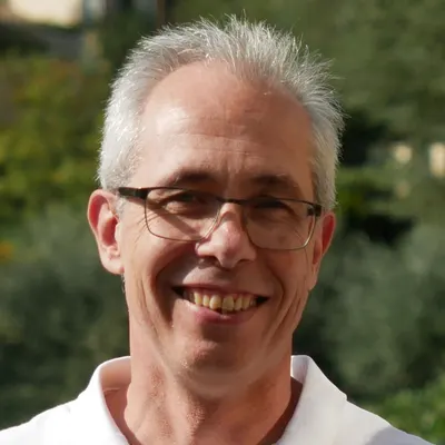 Portrait de Philippe Herzog, en extérieur devant de la végétation.